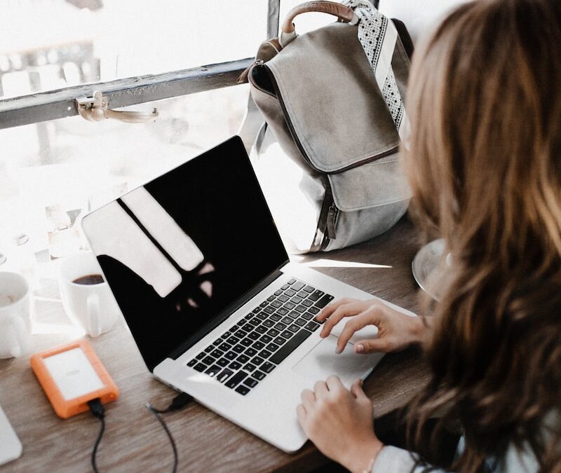 girl wearing grey long-sleeved shirt using MacBook Pro on brown wooden table